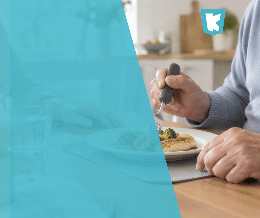 Persona mayor comiendo con un tenedor de mango engrosado en la mesa de su casa